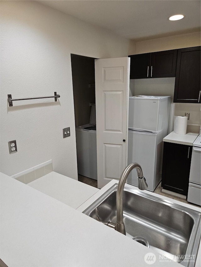 kitchen with light countertops, white appliances, a sink, and dark cabinets