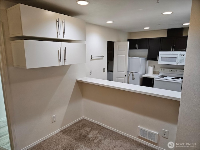 kitchen featuring carpet floors, white appliances, a peninsula, visible vents, and dark cabinetry