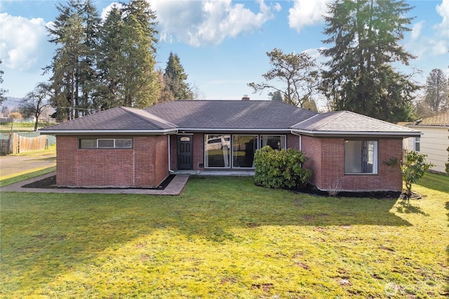 rear view of house with brick siding, a lawn, and fence