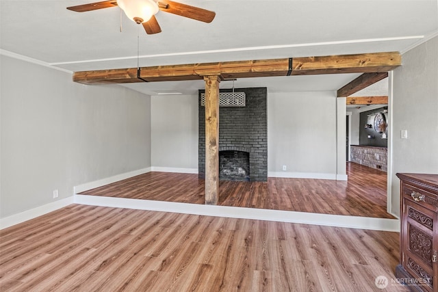 unfurnished living room featuring a brick fireplace, wood finished floors, beam ceiling, and baseboards