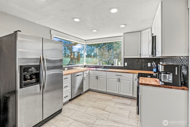 kitchen with a textured ceiling, a sink, wood counters, appliances with stainless steel finishes, and tasteful backsplash