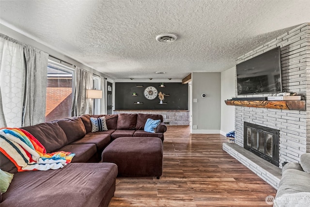 living room featuring baseboards, visible vents, wood finished floors, a textured ceiling, and a fireplace