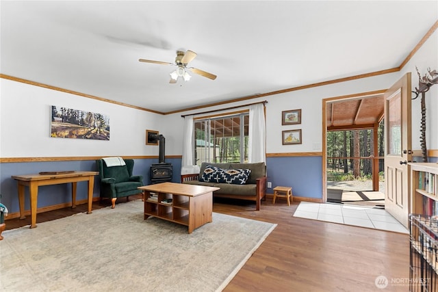 living area with a ceiling fan, wood finished floors, a wood stove, and crown molding