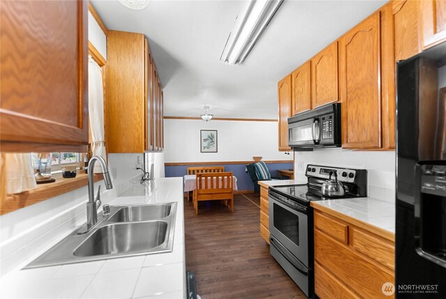 kitchen with tile counters, ornamental molding, dark wood-style flooring, black appliances, and a sink