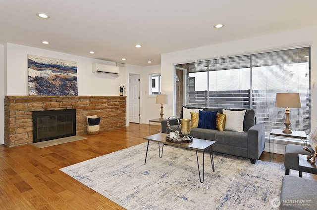 living area with a wall mounted AC, a fireplace, wood finished floors, and recessed lighting