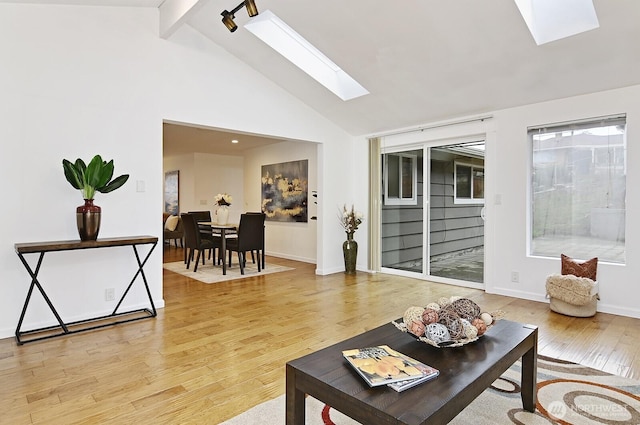 living area featuring a skylight, baseboards, beamed ceiling, light wood-style floors, and high vaulted ceiling