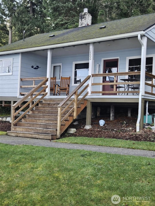 view of front of property with a shingled roof, a chimney, stairs, and a front yard