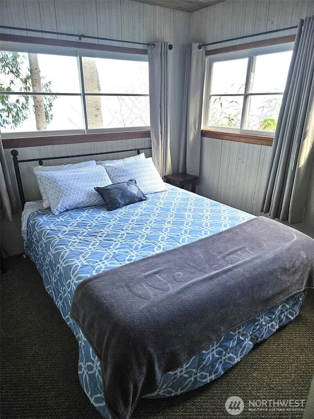 carpeted bedroom featuring wood walls and multiple windows