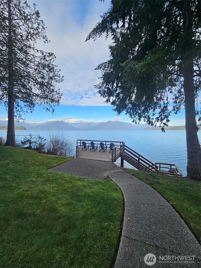 view of dock with a lawn and a water and mountain view