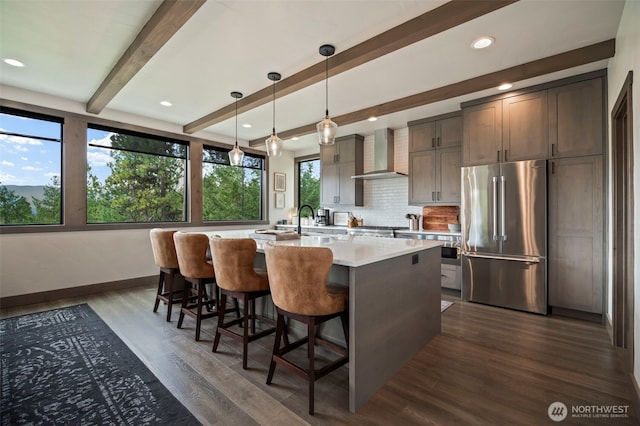 kitchen featuring dark wood finished floors, light countertops, wall chimney range hood, beamed ceiling, and high end refrigerator