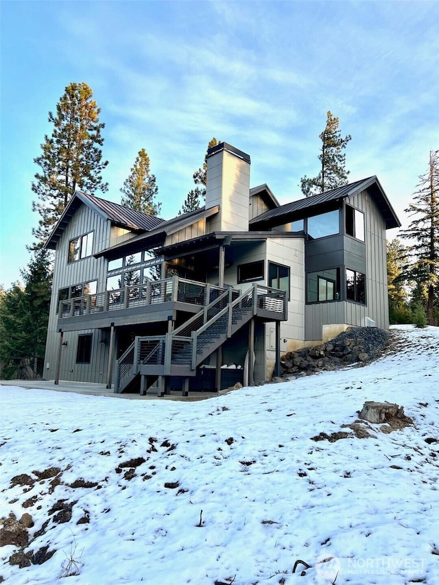 snow covered property with a chimney, stairway, metal roof, a standing seam roof, and board and batten siding