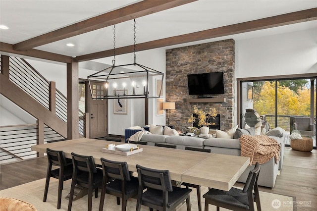 dining area featuring a notable chandelier, a fireplace, wood finished floors, stairway, and beam ceiling