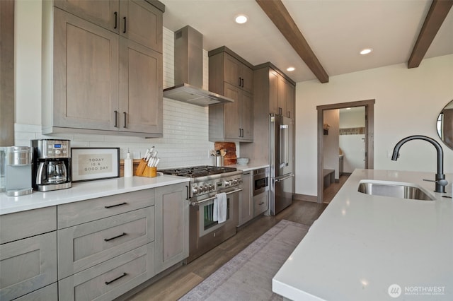 kitchen with a sink, high quality appliances, wall chimney range hood, decorative backsplash, and beamed ceiling