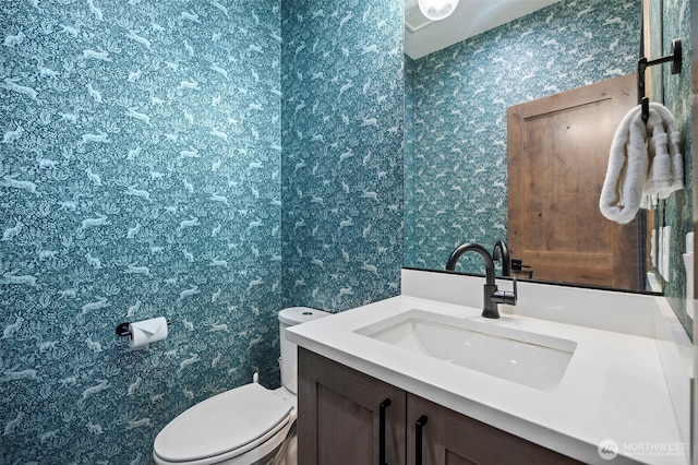 half bath featuring vanity, toilet, and wallpapered walls