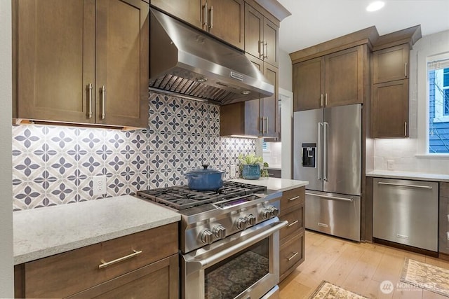 kitchen with premium appliances, light wood-style flooring, under cabinet range hood, decorative backsplash, and light stone countertops