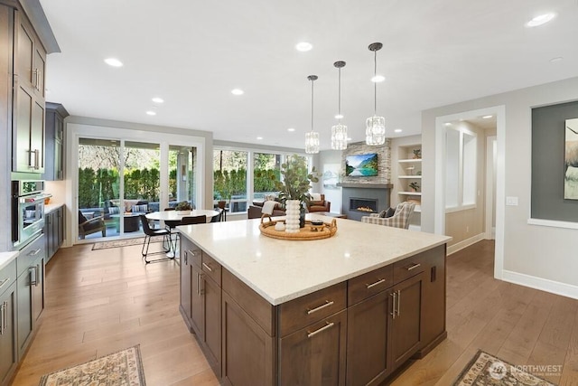 kitchen featuring built in features, recessed lighting, light wood-style floors, stainless steel oven, and a lit fireplace