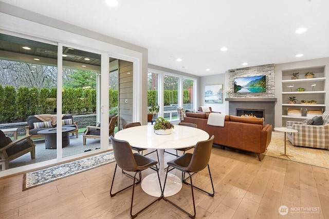 dining room with light wood finished floors, a fireplace, built in shelves, and recessed lighting