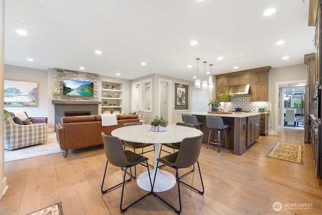 dining room featuring light wood-style floors, a fireplace, built in shelves, and recessed lighting