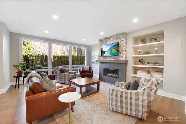 living area featuring a large fireplace, built in shelves, wood-type flooring, and baseboards