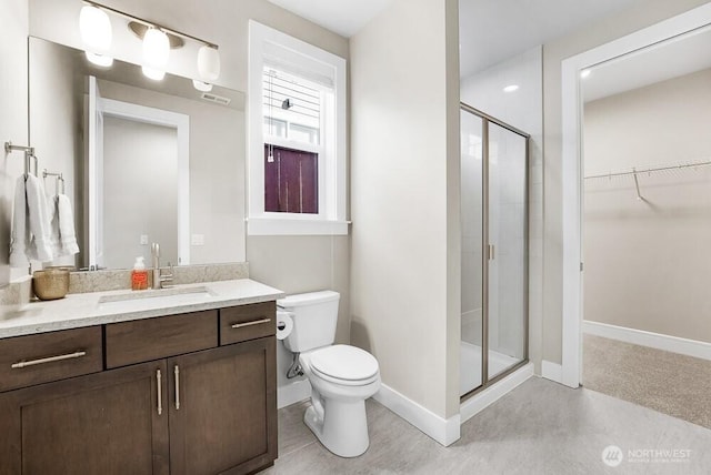 bathroom featuring toilet, vanity, baseboards, a stall shower, and a walk in closet