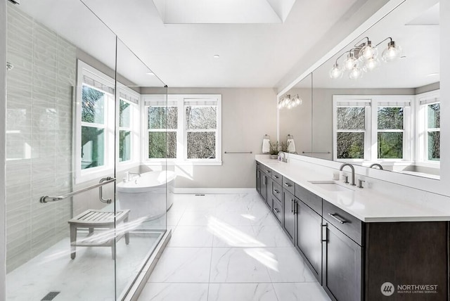 bathroom featuring marble finish floor, a wealth of natural light, a sink, and a soaking tub