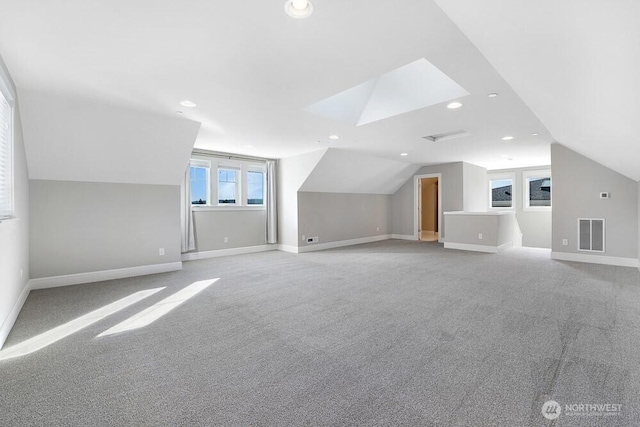 additional living space with vaulted ceiling with skylight, baseboards, visible vents, light colored carpet, and recessed lighting