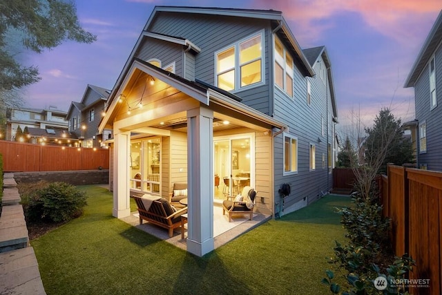 back of house at dusk with a yard, a patio area, and a fenced backyard