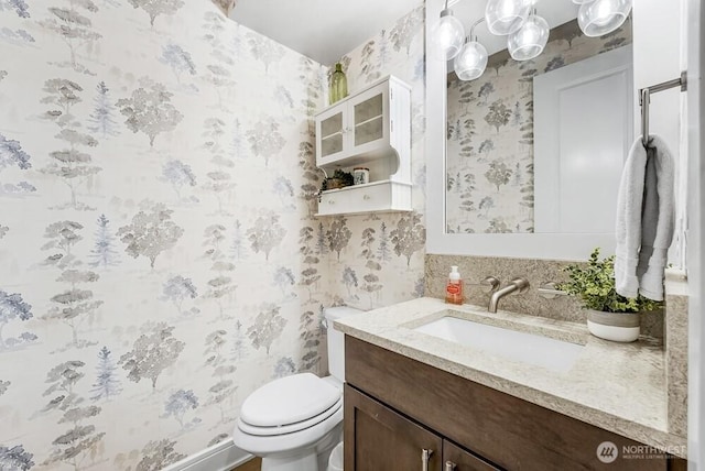 bathroom with vanity, toilet, and wallpapered walls