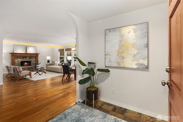 entrance foyer featuring baseboards, arched walkways, wood finished floors, and a fireplace