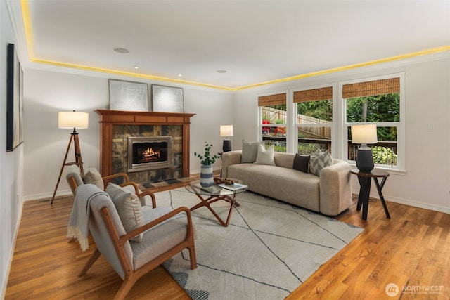 living room with a tiled fireplace, crown molding, wood finished floors, and baseboards