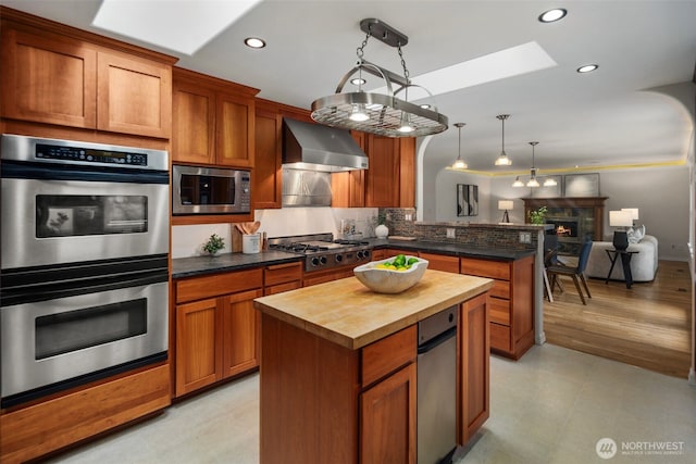 kitchen with butcher block counters, a peninsula, a skylight, stainless steel appliances, and wall chimney exhaust hood