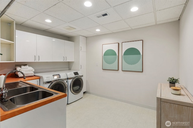 laundry room with light floors, visible vents, washing machine and clothes dryer, cabinet space, and a sink