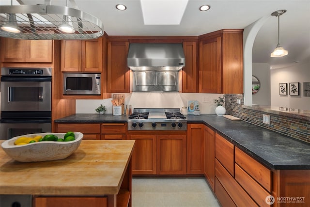 kitchen with butcher block counters, ventilation hood, brown cabinets, and stainless steel appliances