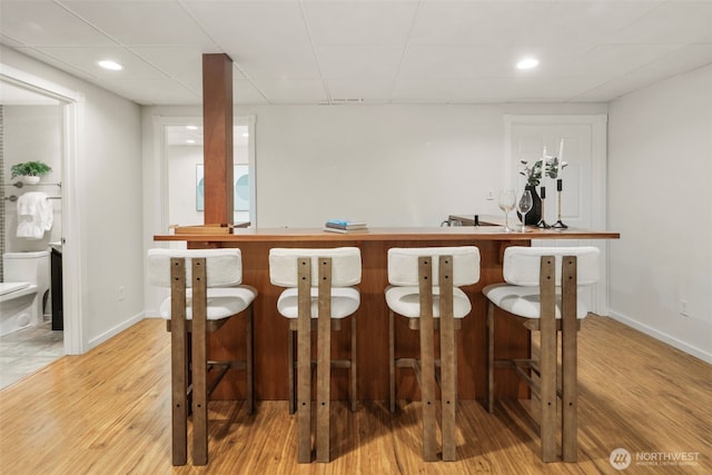 bar with a bar, recessed lighting, baseboards, and light wood-type flooring