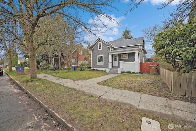 view of front facade with brick siding, roof with shingles, a front yard, and fence