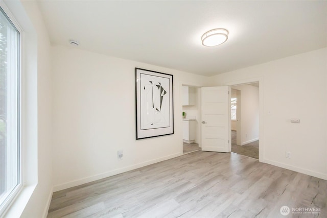 empty room featuring light wood-type flooring, baseboards, and a healthy amount of sunlight