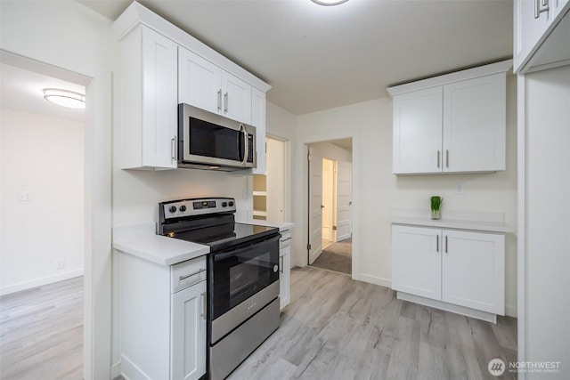 kitchen with baseboards, light countertops, light wood-style flooring, appliances with stainless steel finishes, and white cabinetry