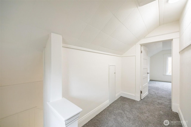 hall with vaulted ceiling, carpet flooring, and baseboards