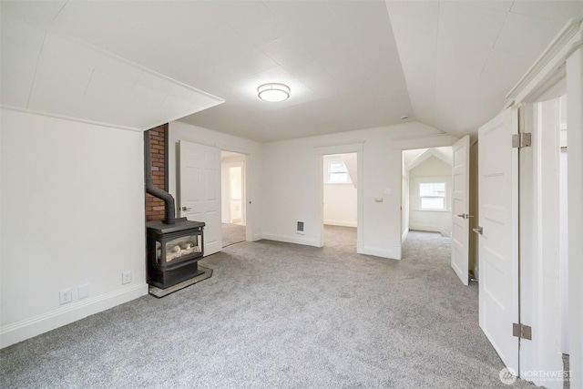 unfurnished living room featuring baseboards, a wood stove, lofted ceiling, and carpet floors