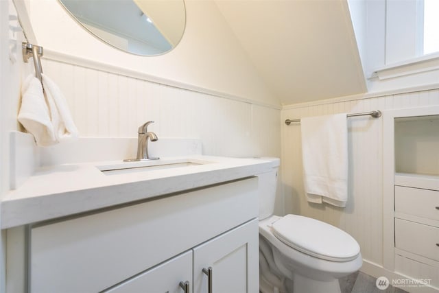 half bathroom featuring toilet, vanity, and vaulted ceiling