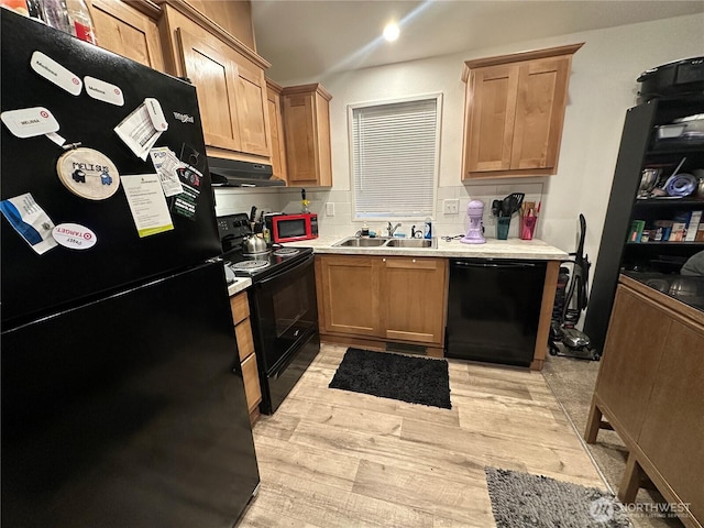 kitchen with under cabinet range hood, a sink, light wood-style floors, light countertops, and black appliances