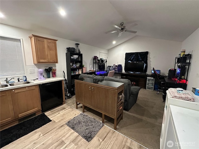 kitchen with a sink, black dishwasher, light countertops, vaulted ceiling, and light wood finished floors