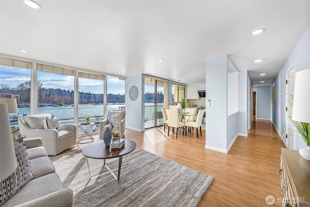 living area with a wall of windows, baseboards, light wood finished floors, recessed lighting, and a water view