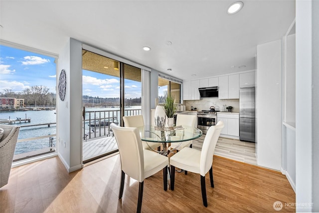 dining area with recessed lighting, light wood-style flooring, a water view, and expansive windows