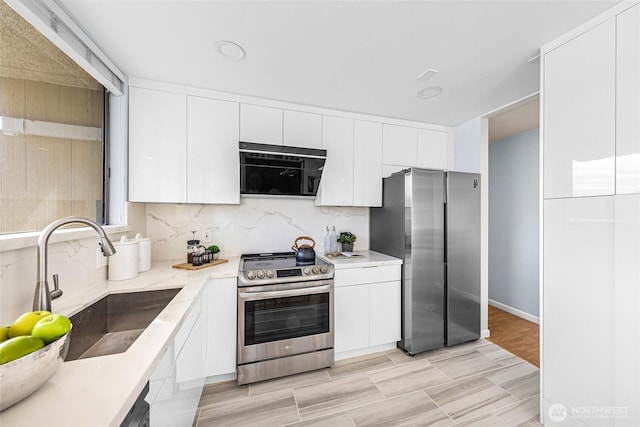 kitchen featuring a sink, white cabinetry, stainless steel appliances, light countertops, and decorative backsplash