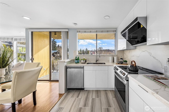 kitchen with a sink, stainless steel appliances, light countertops, white cabinetry, and tasteful backsplash