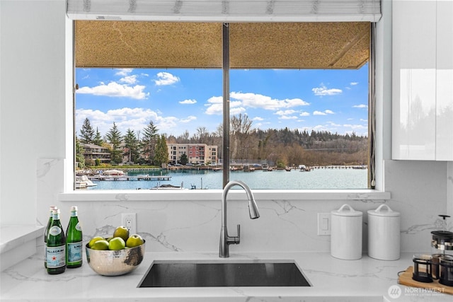 kitchen featuring white cabinetry, decorative backsplash, a water view, and a sink