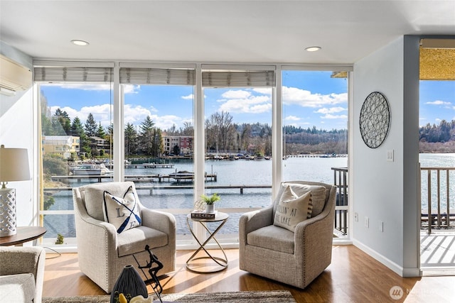 sitting room featuring a wall of windows, a water view, a healthy amount of sunlight, and wood finished floors