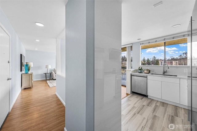 kitchen with light wood-type flooring, light countertops, stainless steel dishwasher, white cabinetry, and a sink