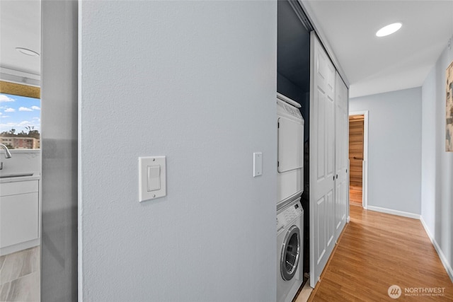 clothes washing area with light wood-style flooring, stacked washer / drying machine, and baseboards